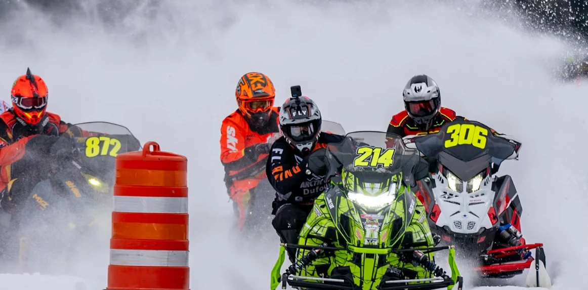 TJ Leach racing an Arctic Cat snowmobile through a pack in flying snow